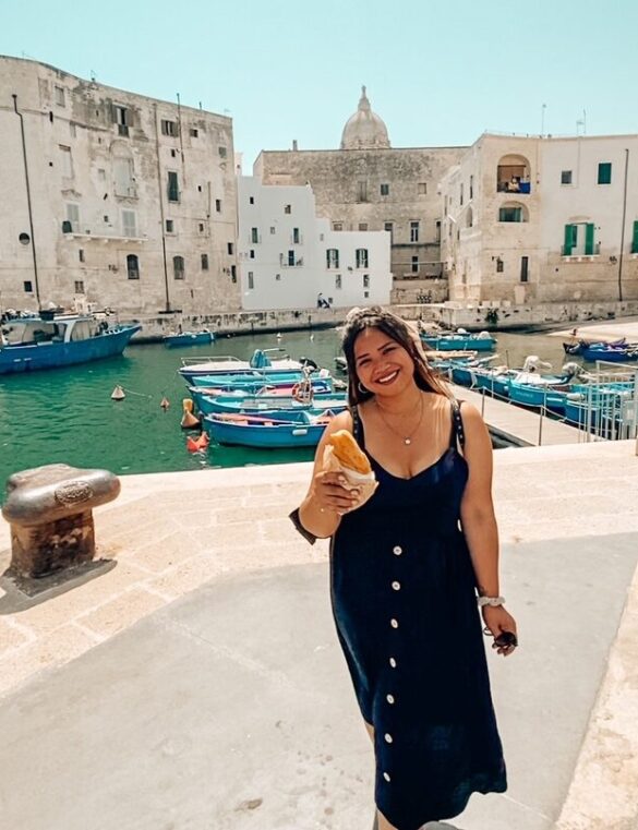 ragazza sorride mentre mangia un panzerotto pugliese nel porto antico di Monopoli in Puglia