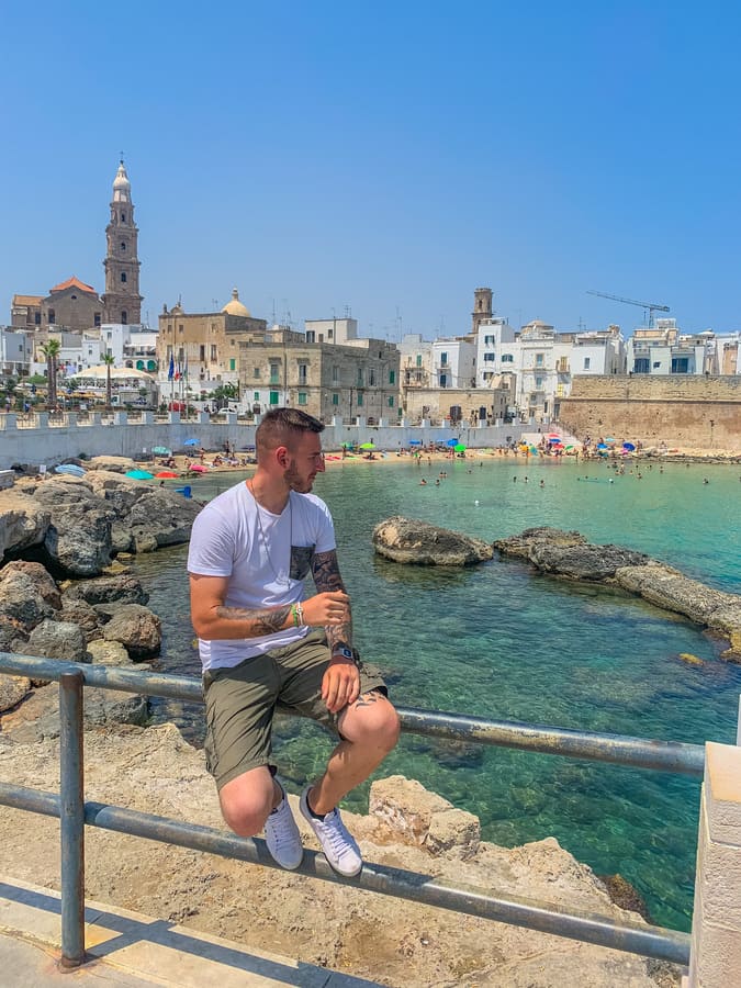 Ragazzo seduto sulla staccionata ammira la spiaggia più bella di Monopoli in Puglia