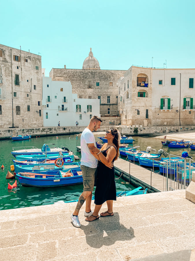 coppia si guarda negli occhi nel bellissimo porto antico di Monopoli con le barche colorate e edifici storici da vedere in un giorno